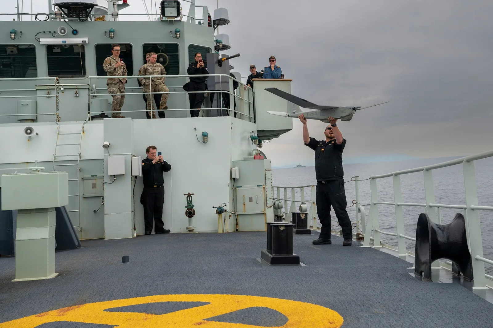 Royal Canadian Navy sailor holding a CU-175 Puma drone above his head on a ship’s deck before launch.