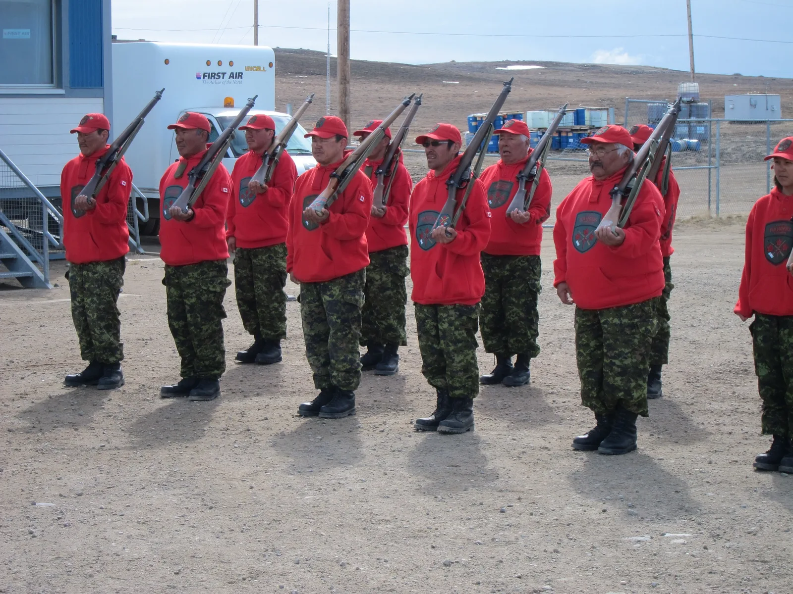Canadian Rangers in red uniforms carrying rifles in formation in Nunavut, Canada.