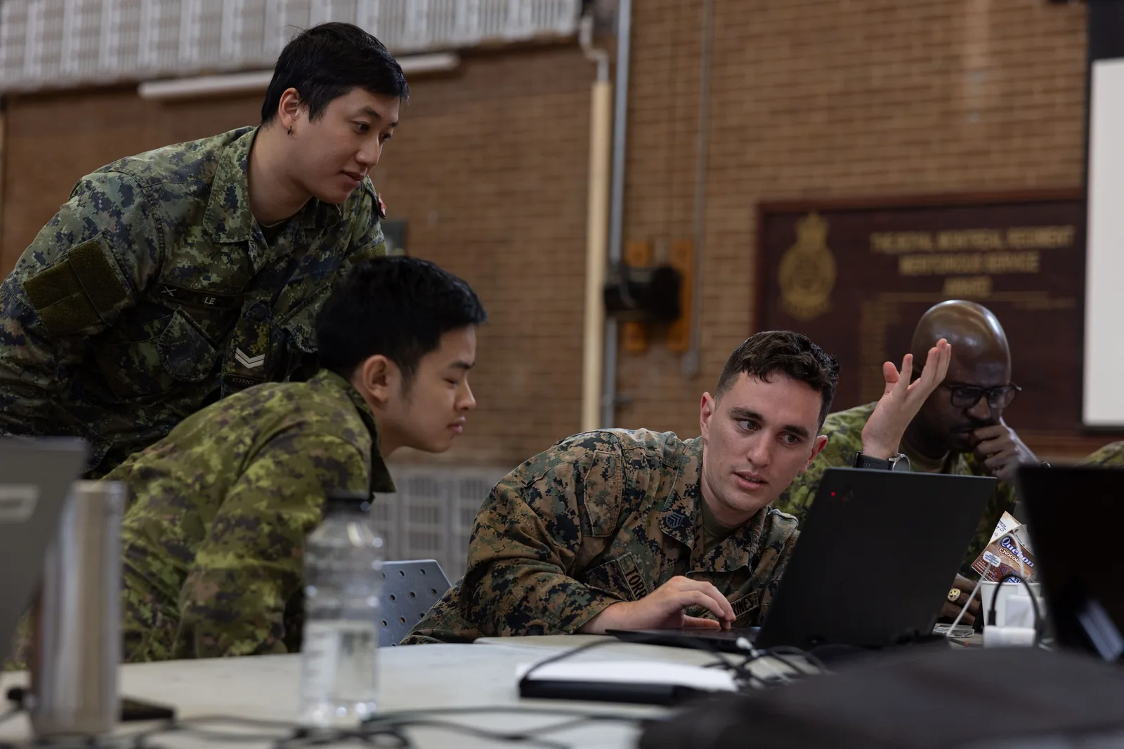 Canadian Army personnel and a U.S. Marine work together around laptops during Cyber Harmony 24 in Montreal.