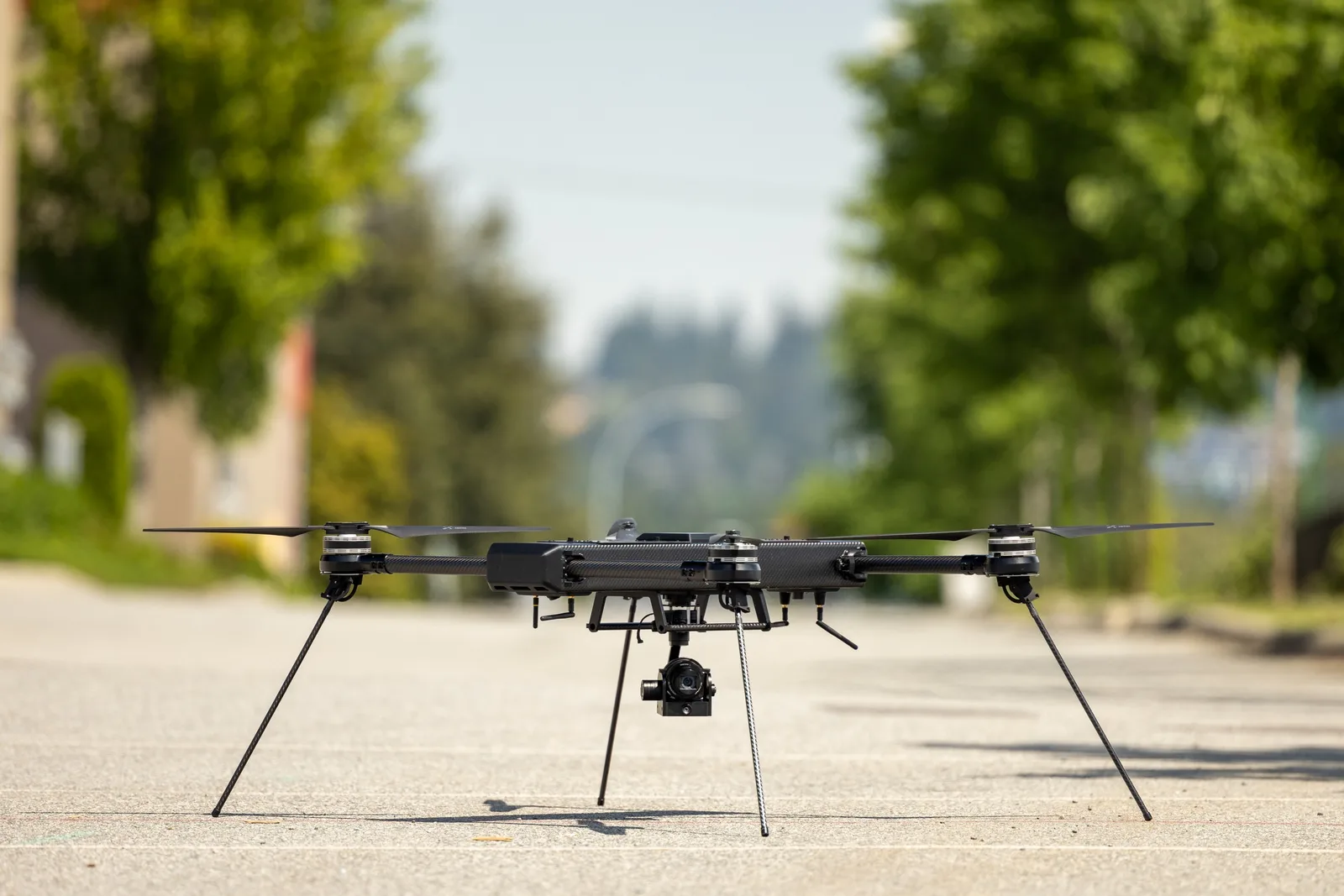 A Draganfly Commander 3XL quadcopter with a camera payload stands on a paved road.