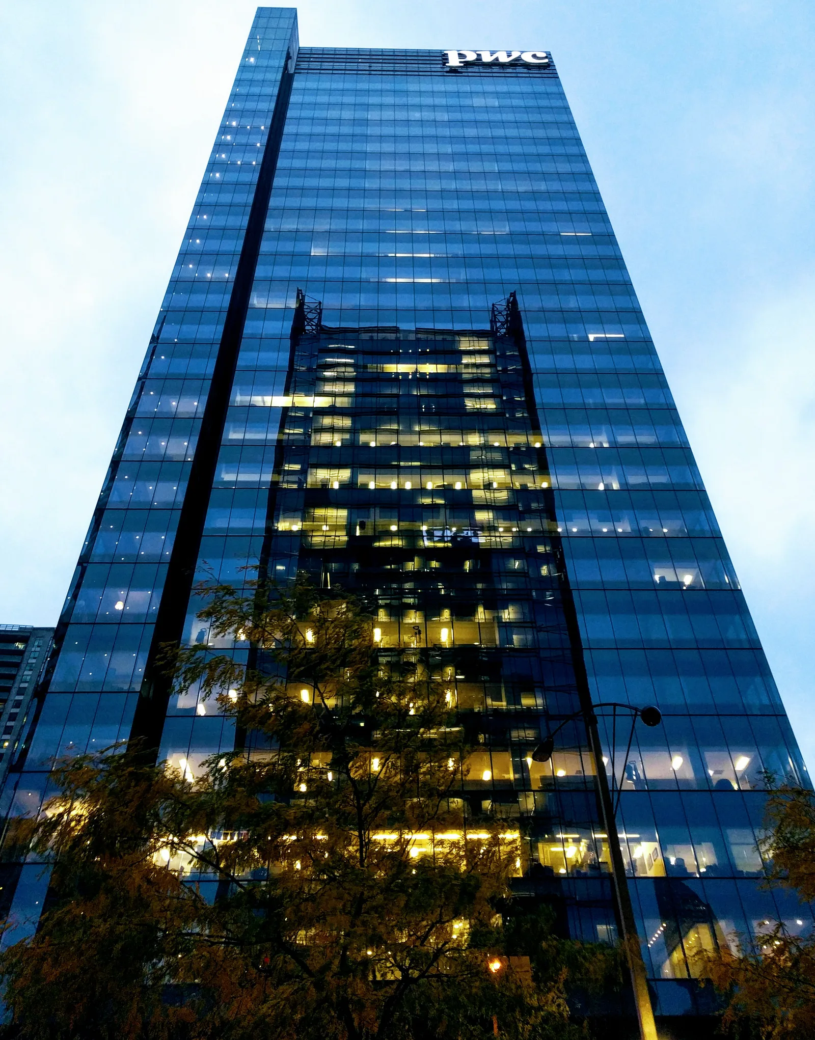 PwC signage near the top of a blue glass office tower in Toronto.
