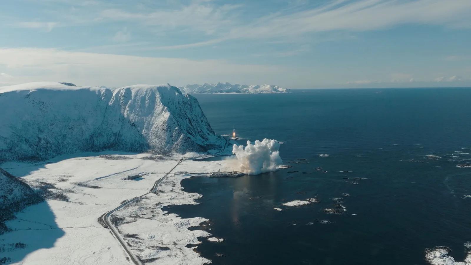 Aerial photograph of Spectrum lifting off beside snow-covered mountains and the sea at Andøya Spaceport in Norway.