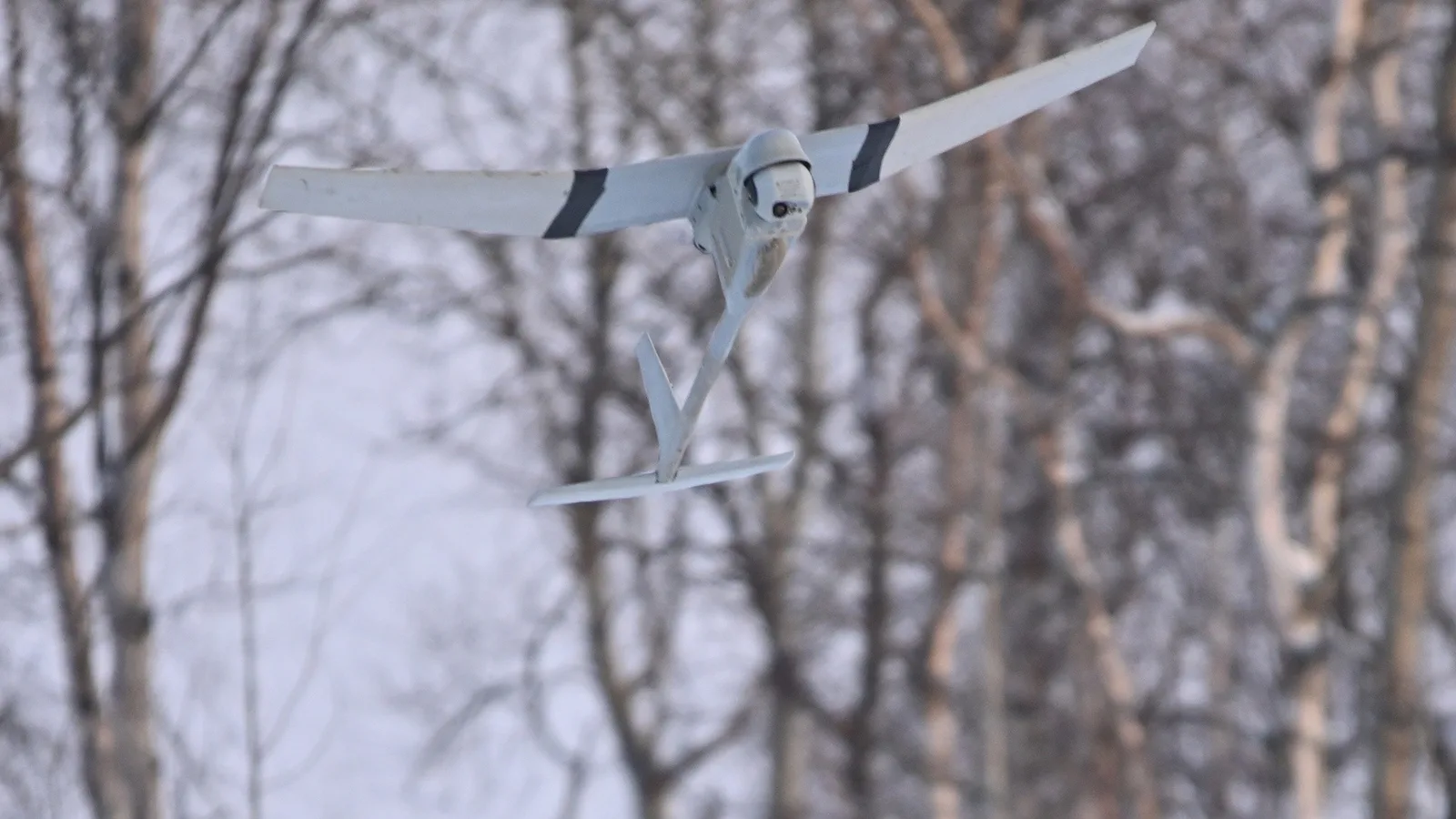 A U.S. Army Raven drone flies after launch above snow-covered trees in Alaska in 2023.